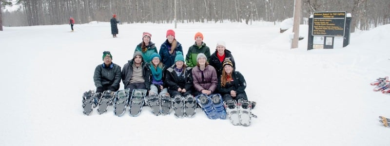 row of students sitting with feet toward you, all have snowshoes on