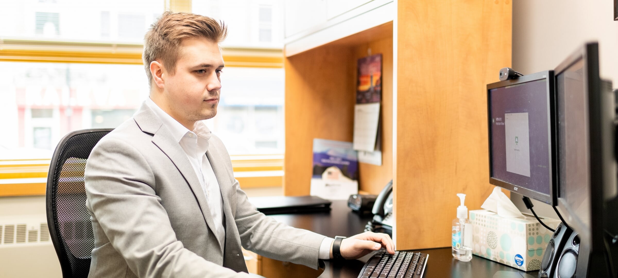 Student in a suit sitting at a dual-screen computer.