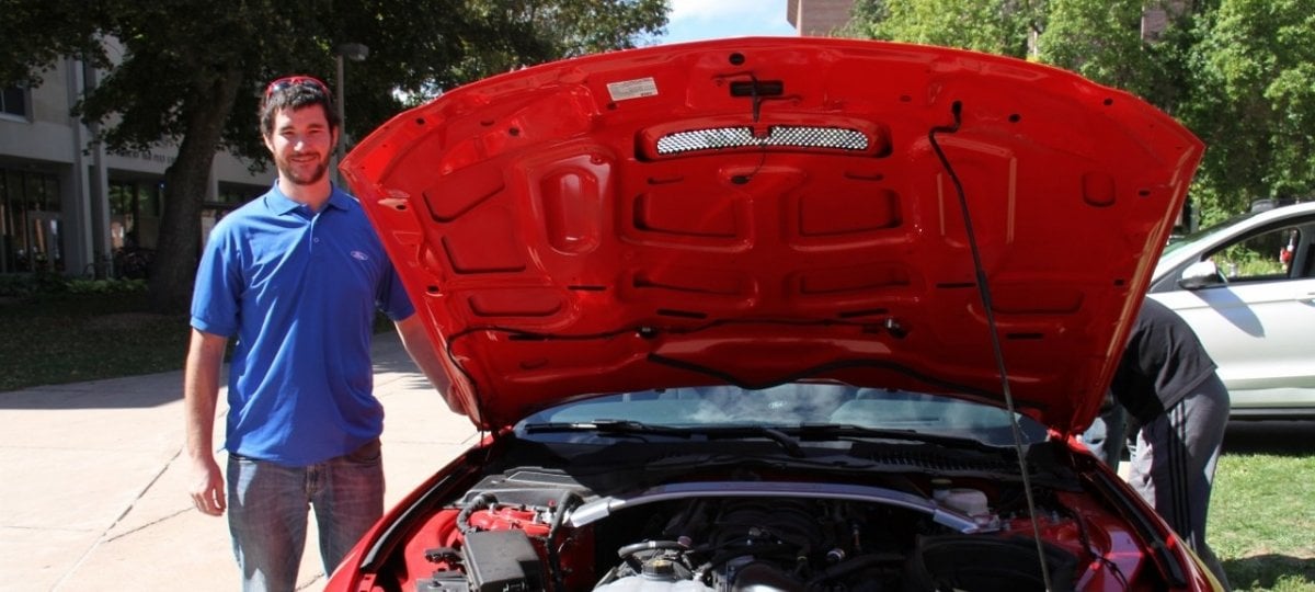 Researcher standing next to a car with the hood open.