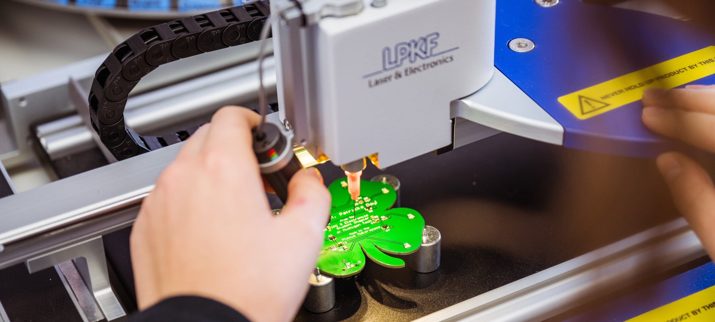 Closeup of a student making a shamrock-shaped circuit board on a laser cutting machine.