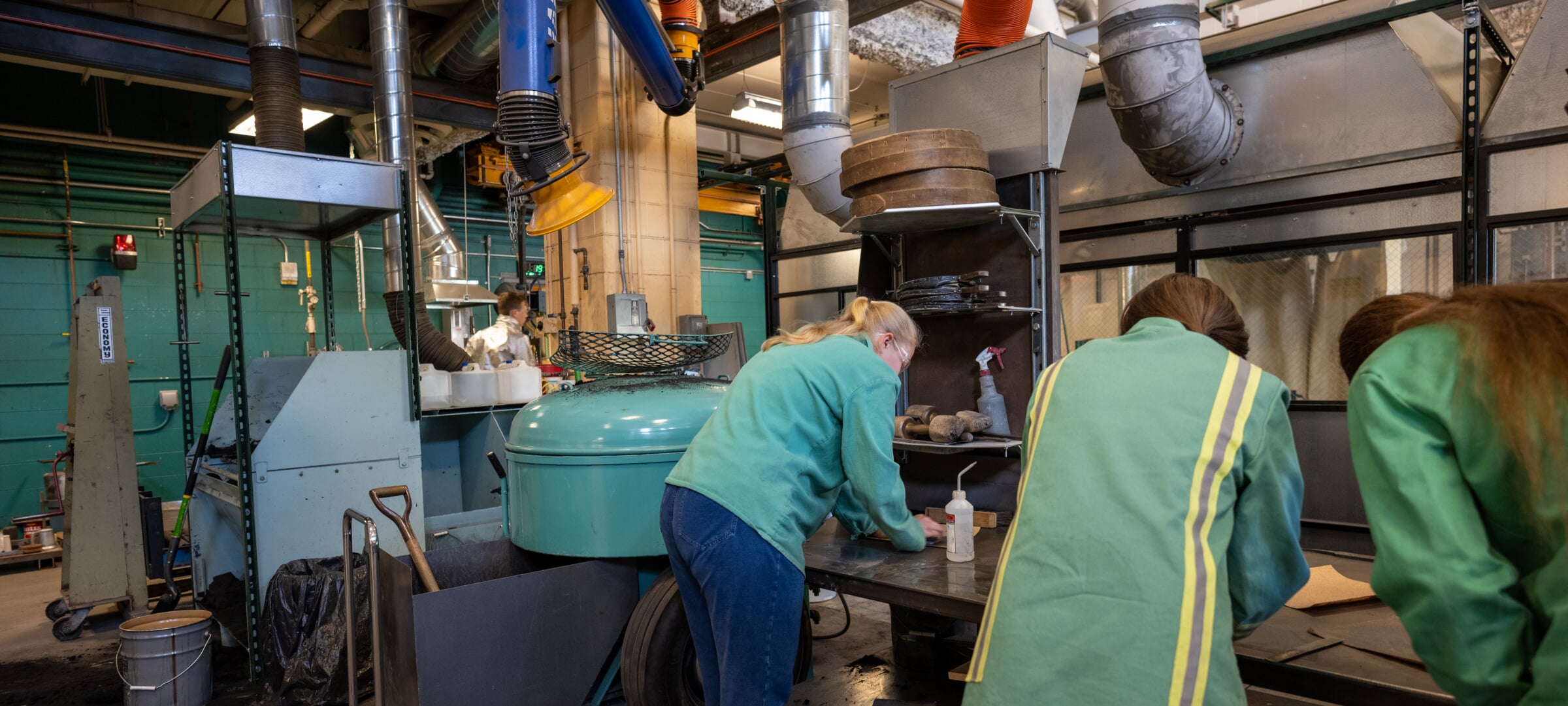 Students bent over a table next to some machinery, working in the materials and manufacturing lab.