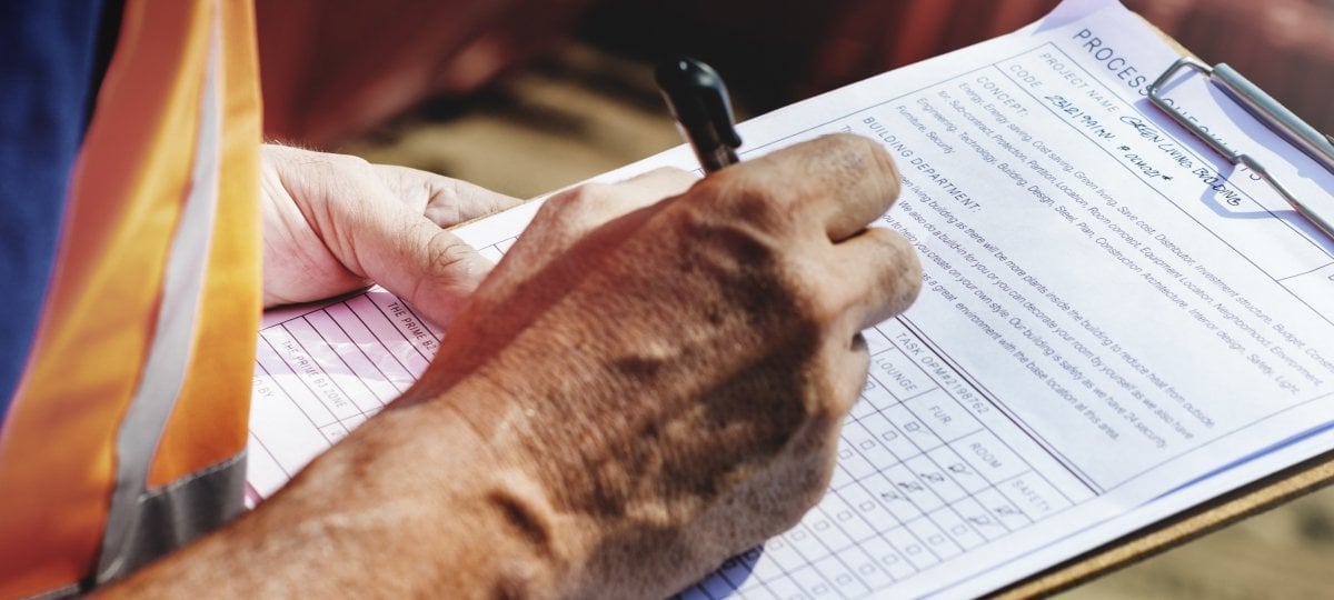 Worker with vest writing on a clipboard with form.