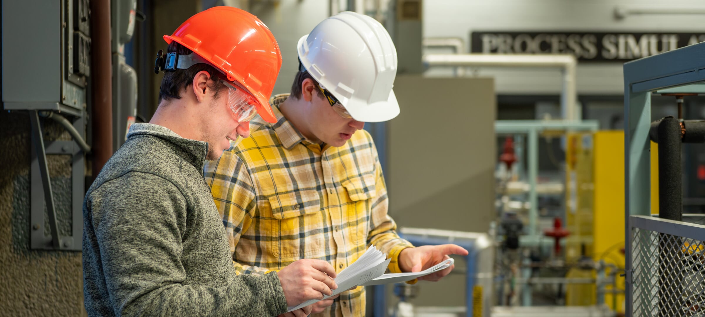 Students wearing hardhats inspect paperwork in front of machinery.
