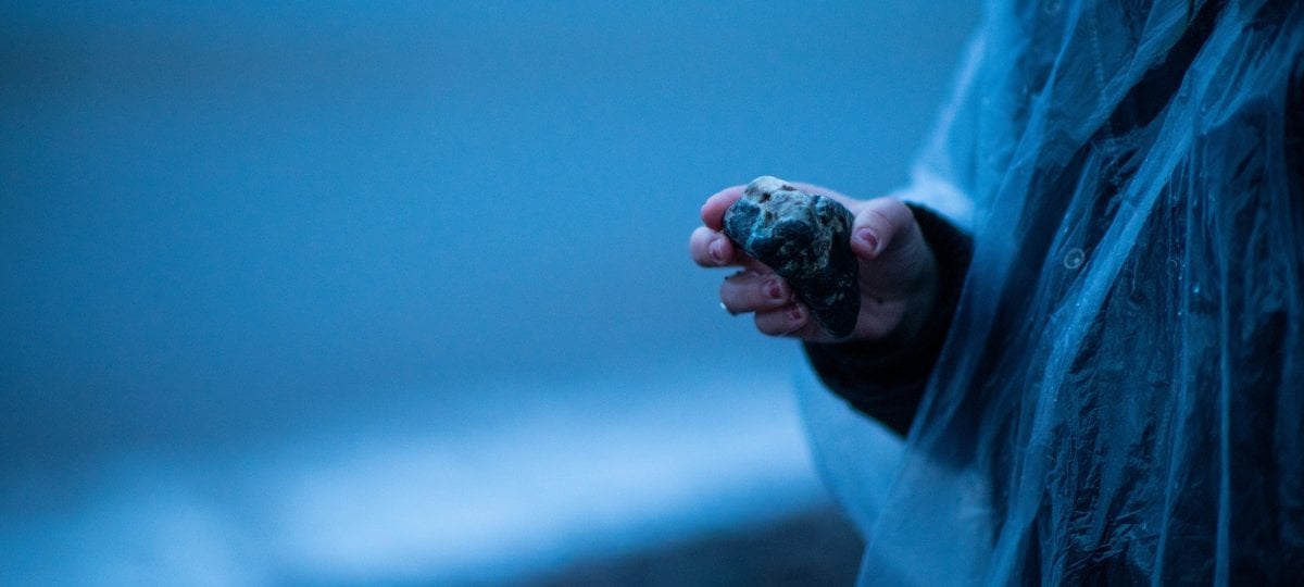 Person in raincoat by a lake holding a rock.