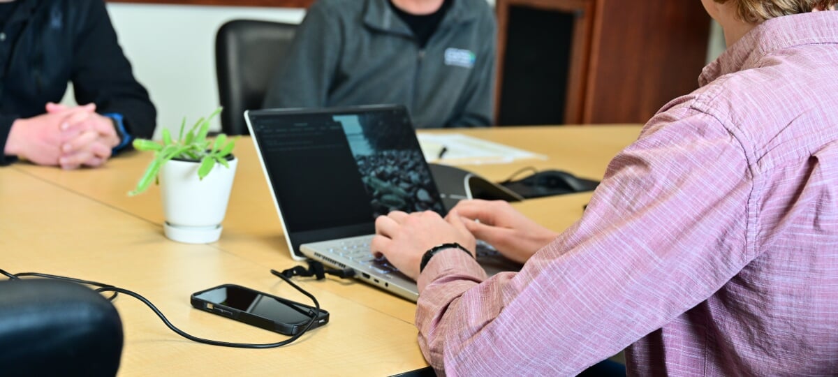 Student typing on a laptop at a table with other students.