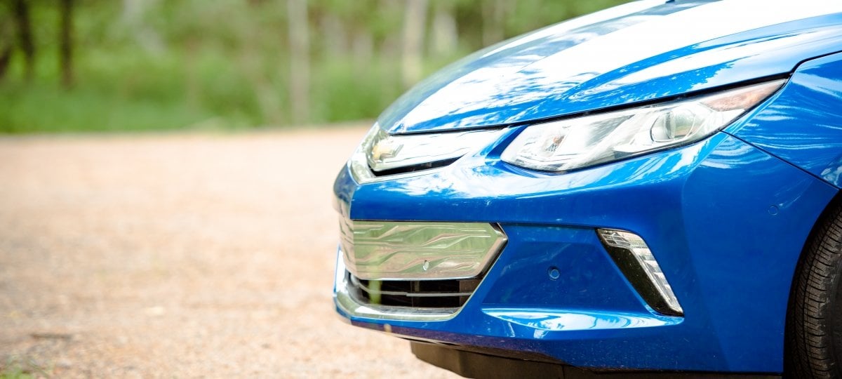 Front section of a parked car on a dirt road in the woods.