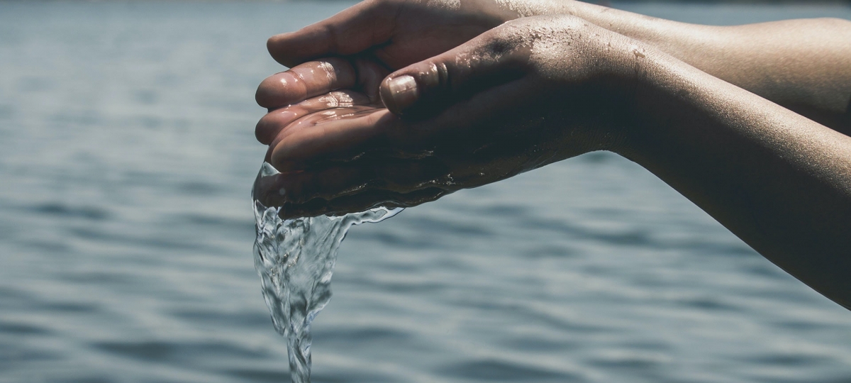 Hands holding water as it falls by a lake.