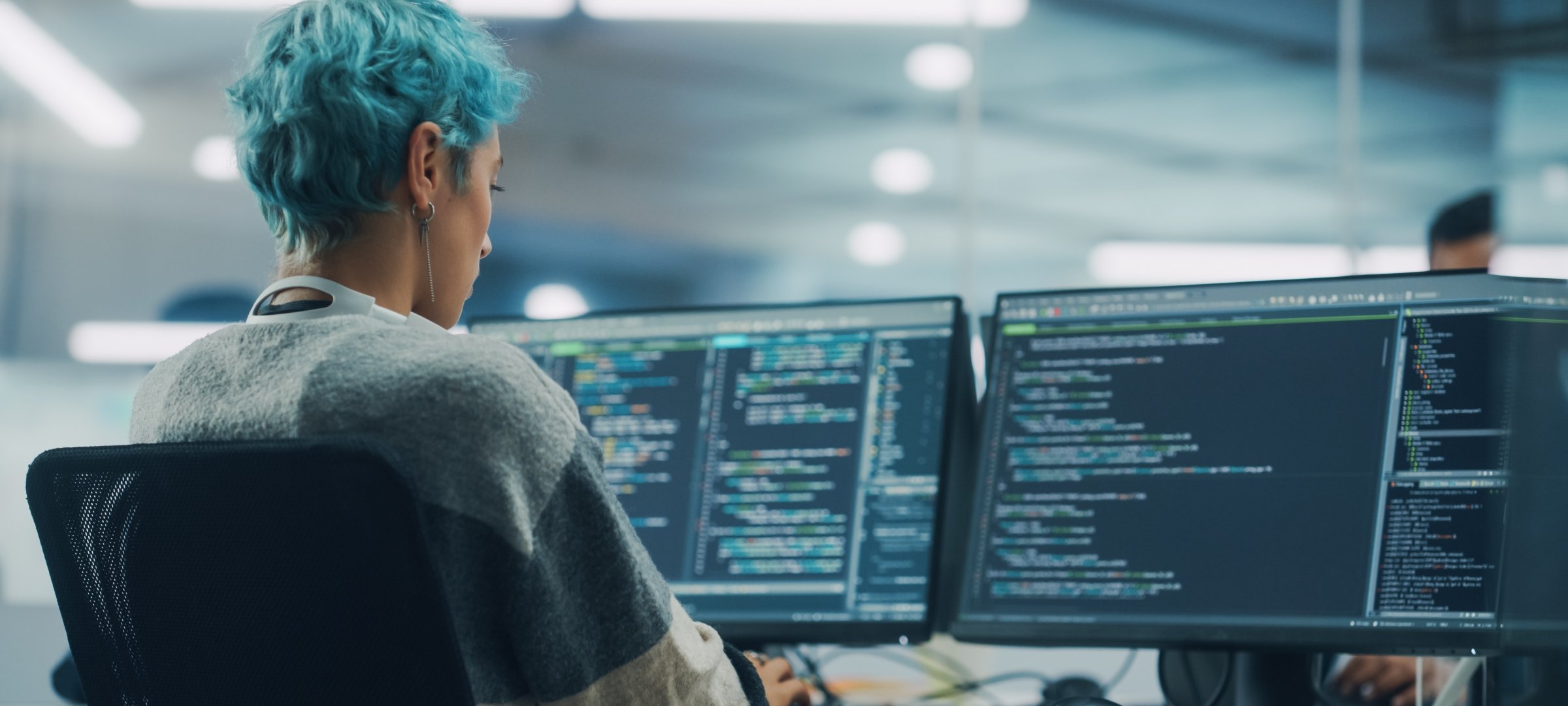 Grad student sitting writing code with two monitors.