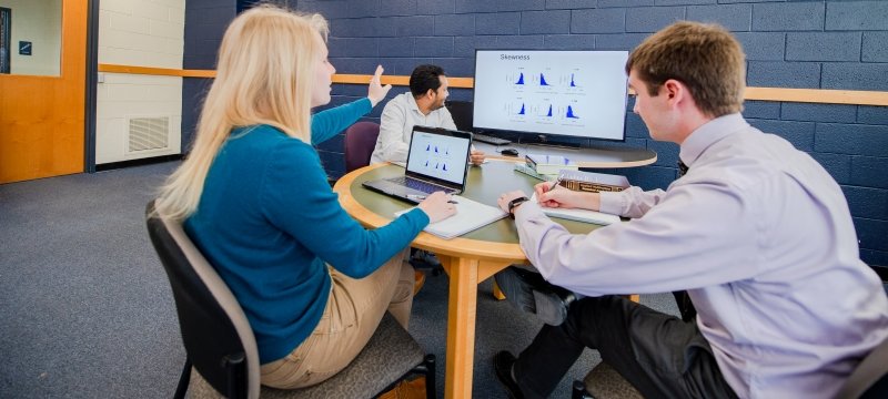 Three grad students sitting around a table looking at graphs on computer screens.