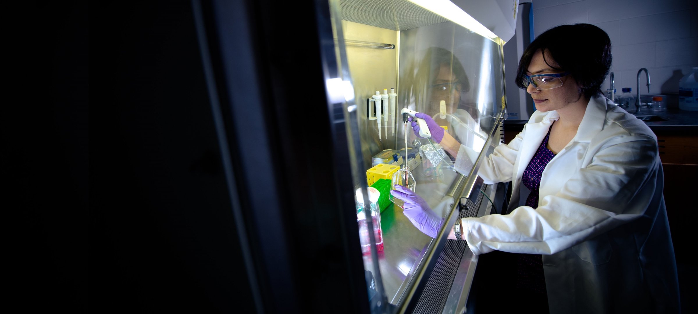 Grad student working in safety gear working with chemicals under a hood in a lab.