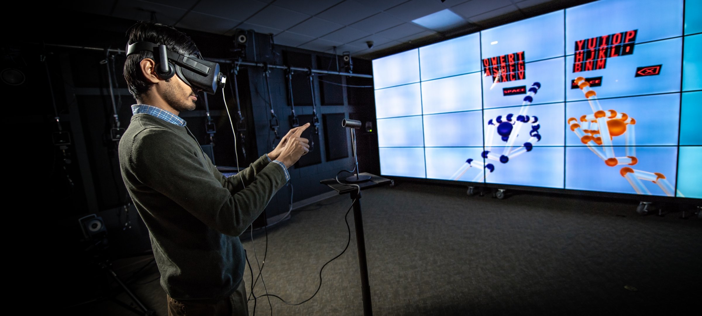 Grad Student with VR headset standing in front of large VR screen with hands raised