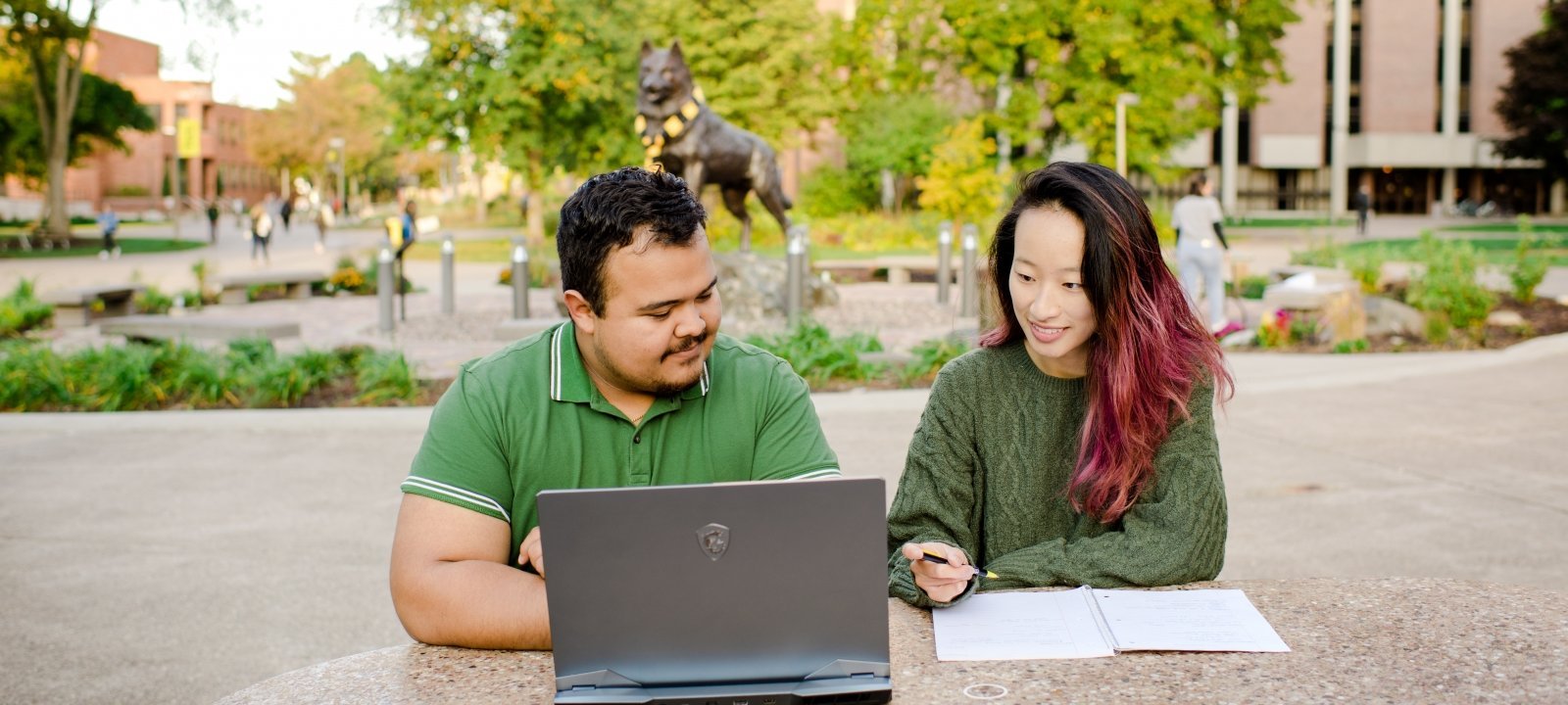 Three students working around a a laptop on a desk.