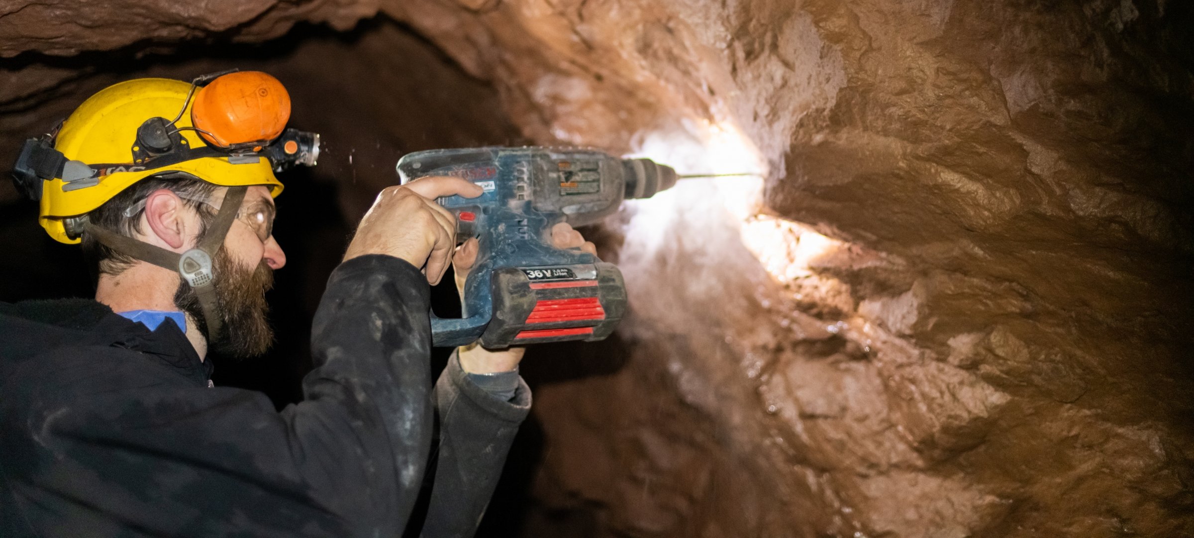 Researcher in Mead Mine with safety glasses and hard hat drilling into rock.