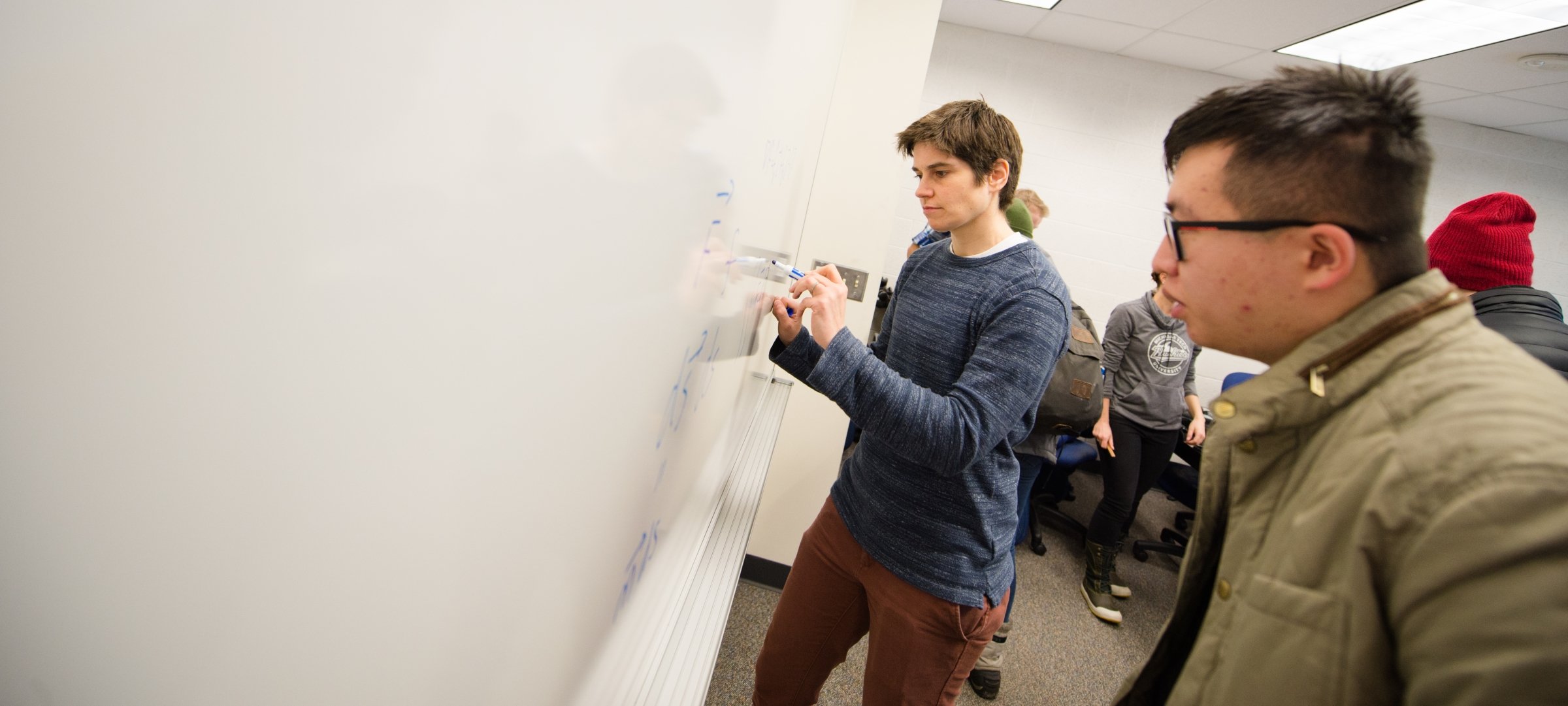 Dry whiteboard with faculty writing and grad student looking on.