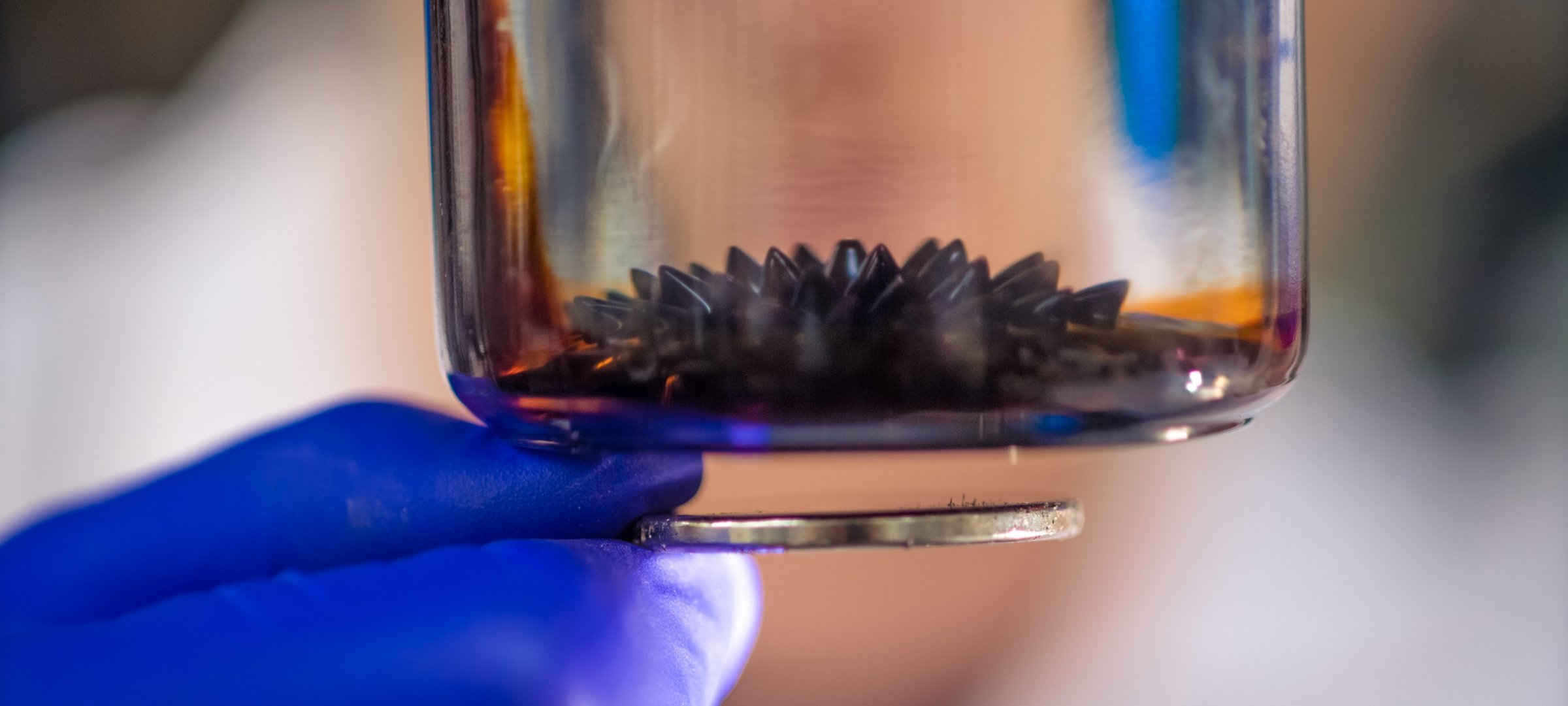 Researcher holding a beaker with ferrofluid research for satellites.