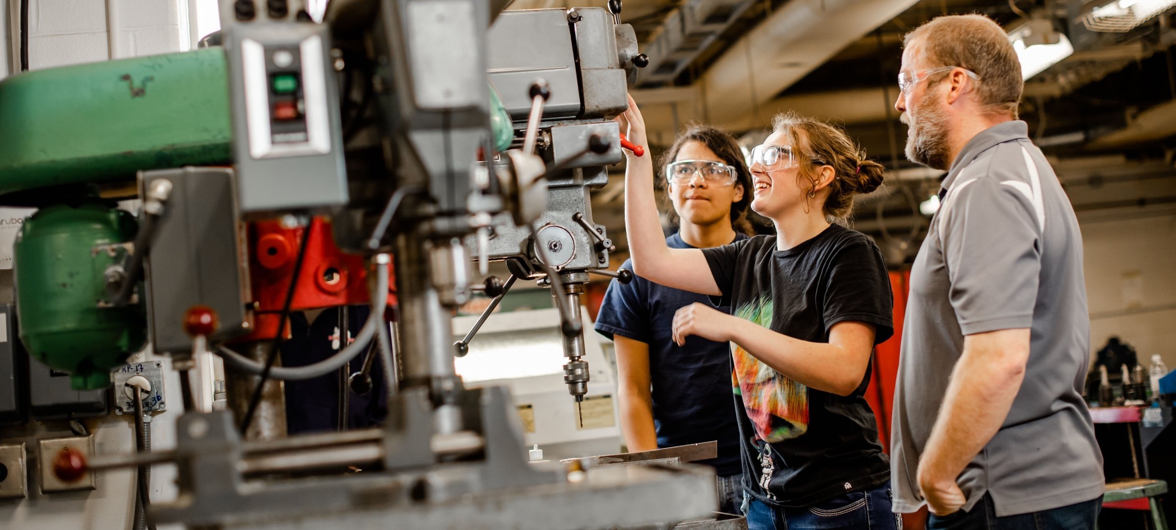 Three grad students in a machine shop operating a drill