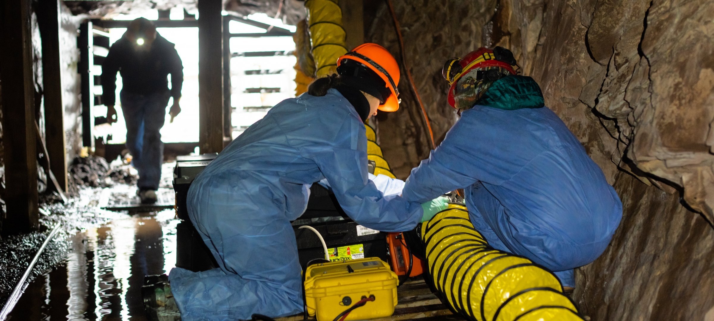 Mining engineering students inside Mead Mine working on hoses in jumpsuits and hardhats.