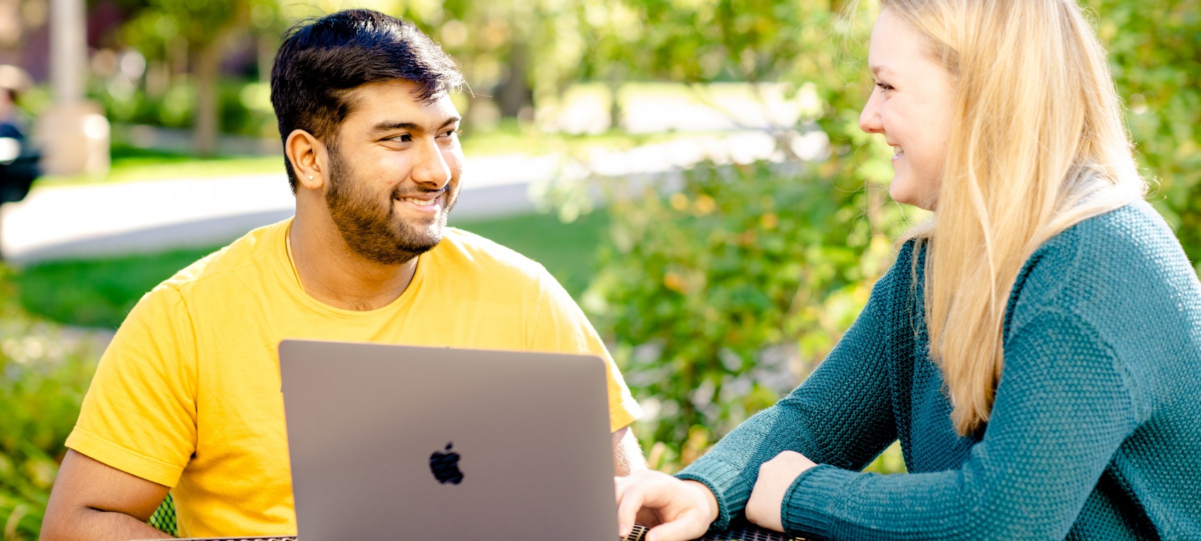 Two grad students talking outside with a laptop.