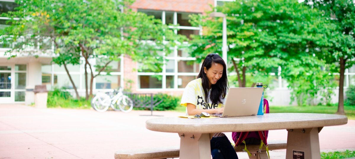International student sitting outside the Dow at a table with laptop smiling