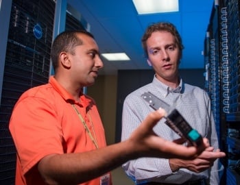 Faculty talking with student between 2 huge computing banks of equipment.