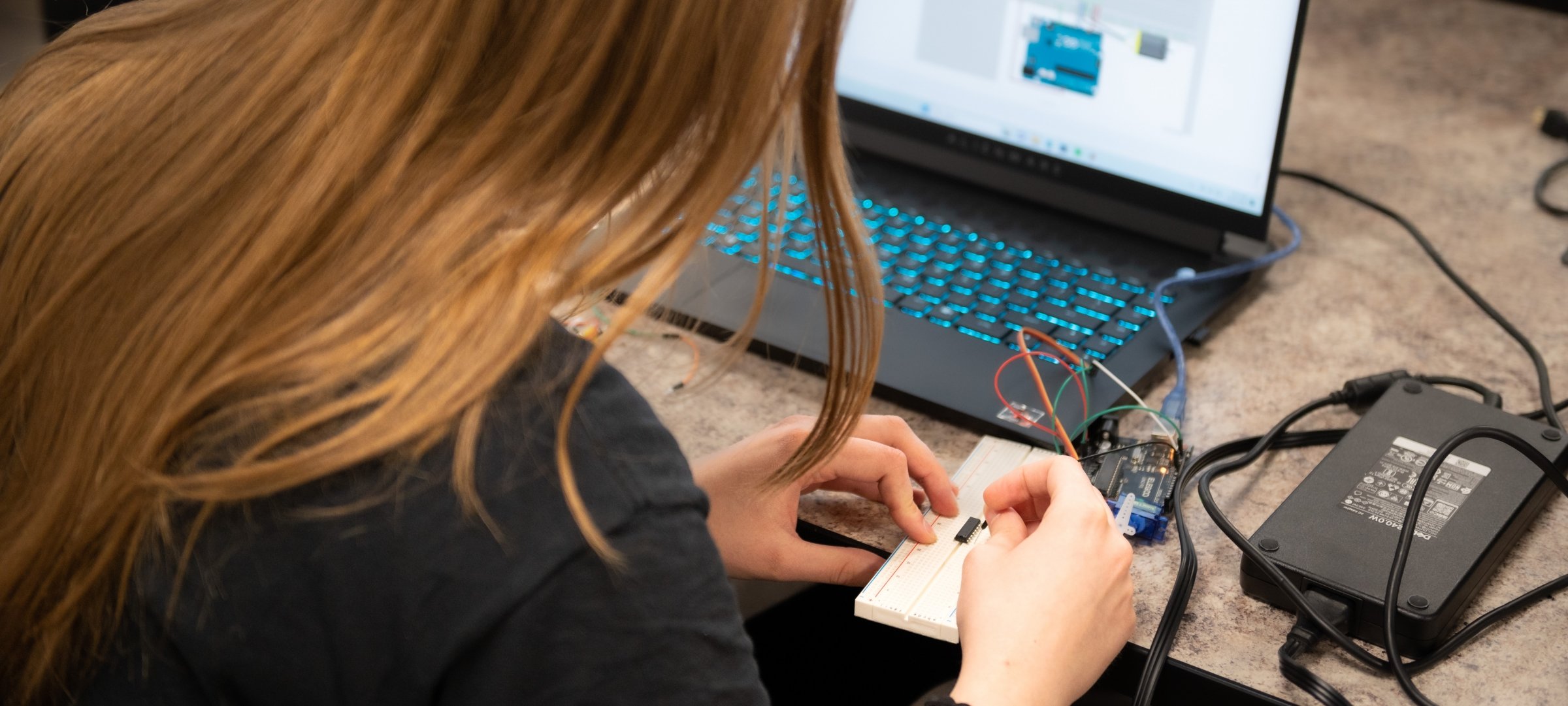 Engineering Student working on a device with a laptop.