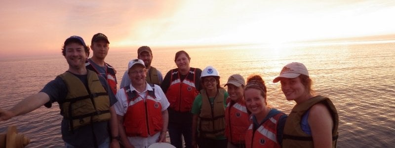 Graduate students posing for a photo on a research vessel on the water during sunset