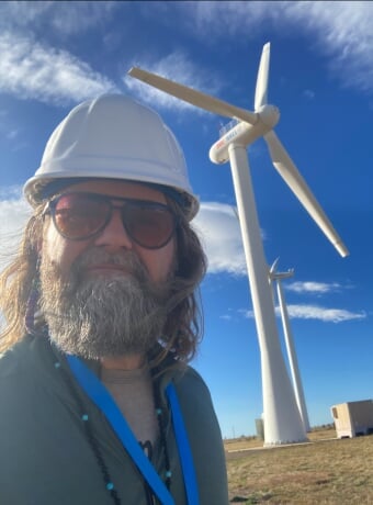 Weston Eaton wears a hardhat with a wind turbine in the background.