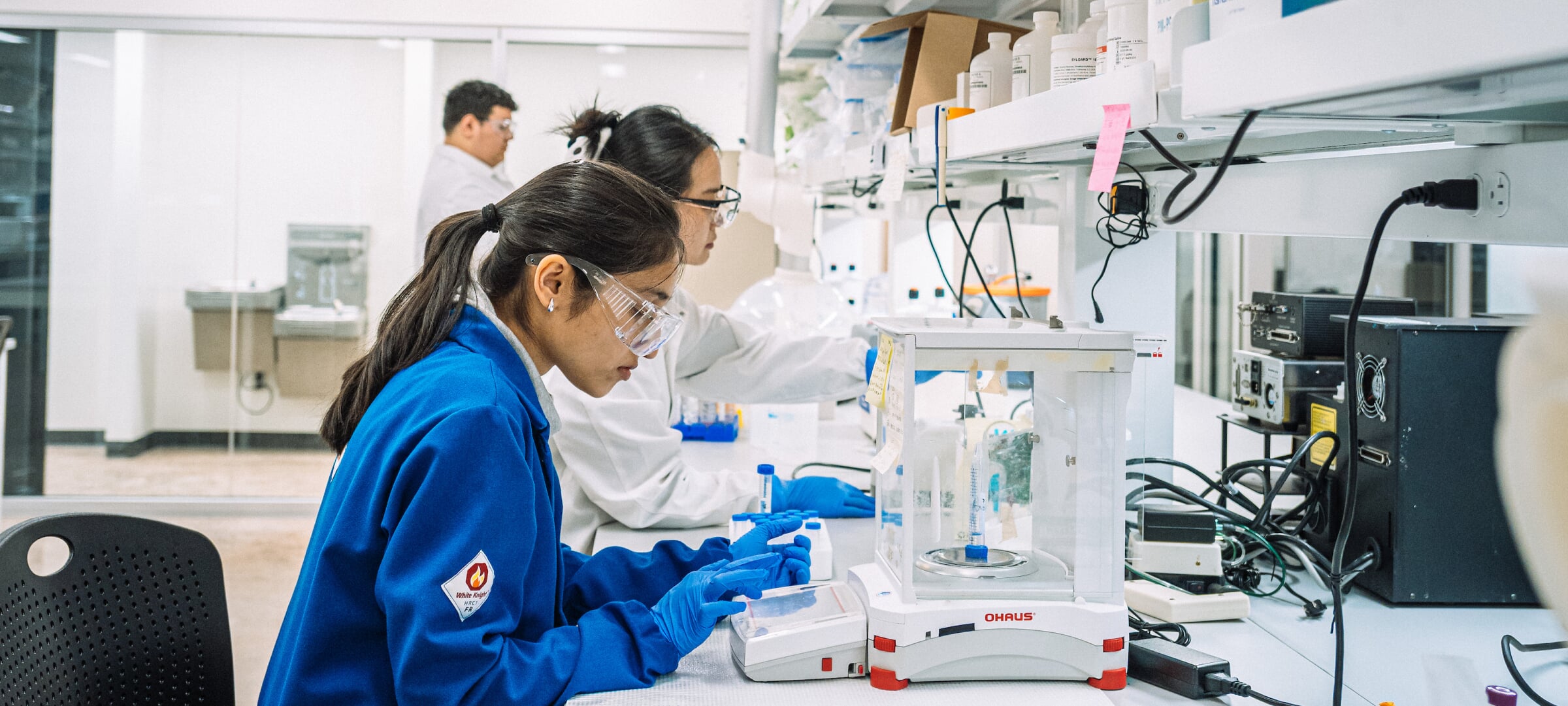 Graduate students doing research in a lab with lab coats, gloves, and glasses.