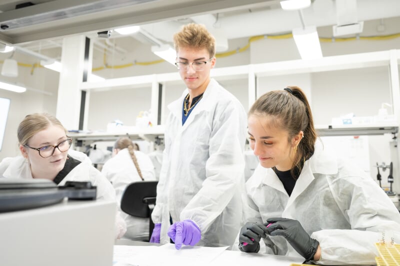 Three students in a lab with lab coats.