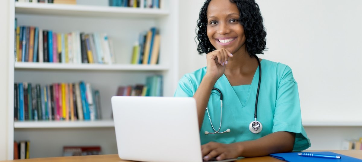 A woman in scrubs sitting at a desk with laptop