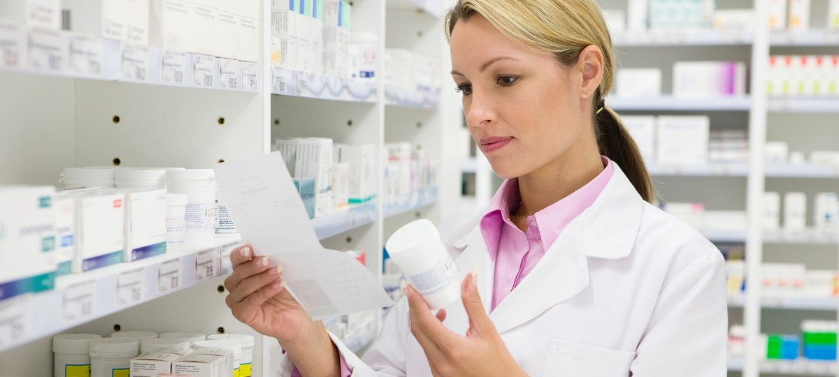 A woman doctor reads a pill bottle in a pharmacy