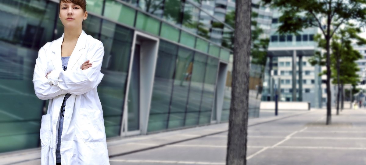 A woman in a lab coat stands outside a building