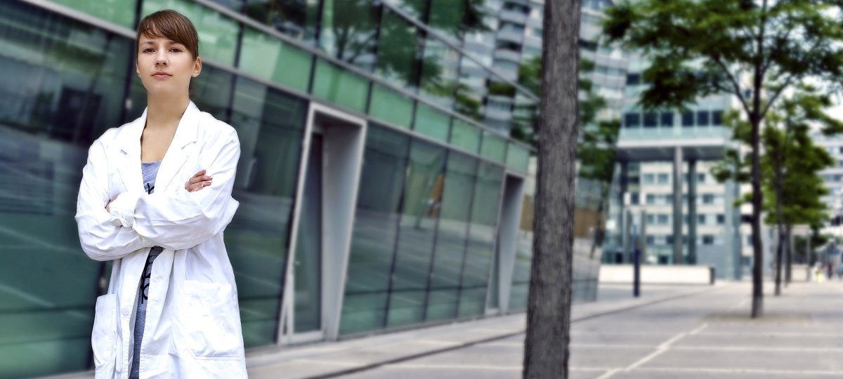 Woman in lab coat standing outside a glass building.