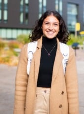 Student, Jillian, with long jacket and backpack standing outside smiling