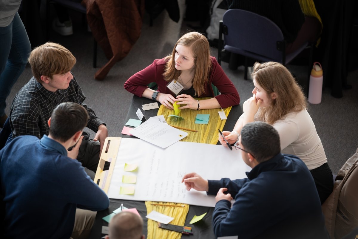 Students gathered around a table with large sheets of paper discussing their project