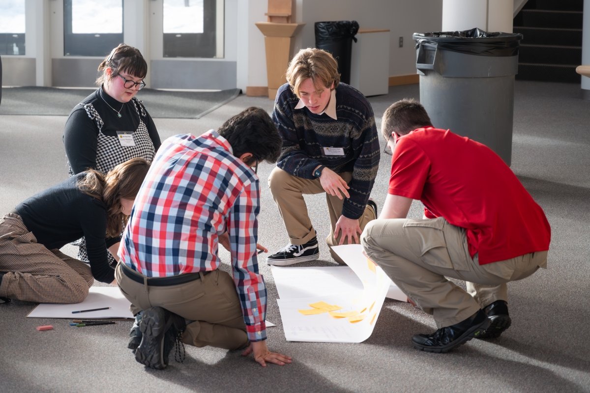 Students kneeling on the floor working on their poster for the presentation.