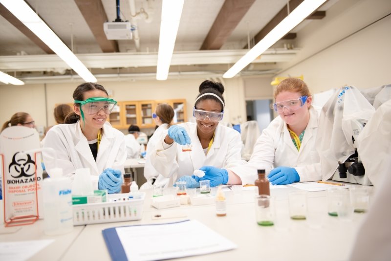 Three SYP students with lab coats and PPE doing an experiment.