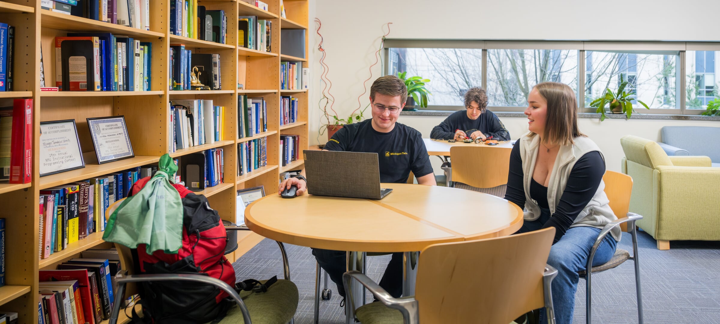 students studying at round tables with a wall of bookshelves to their left