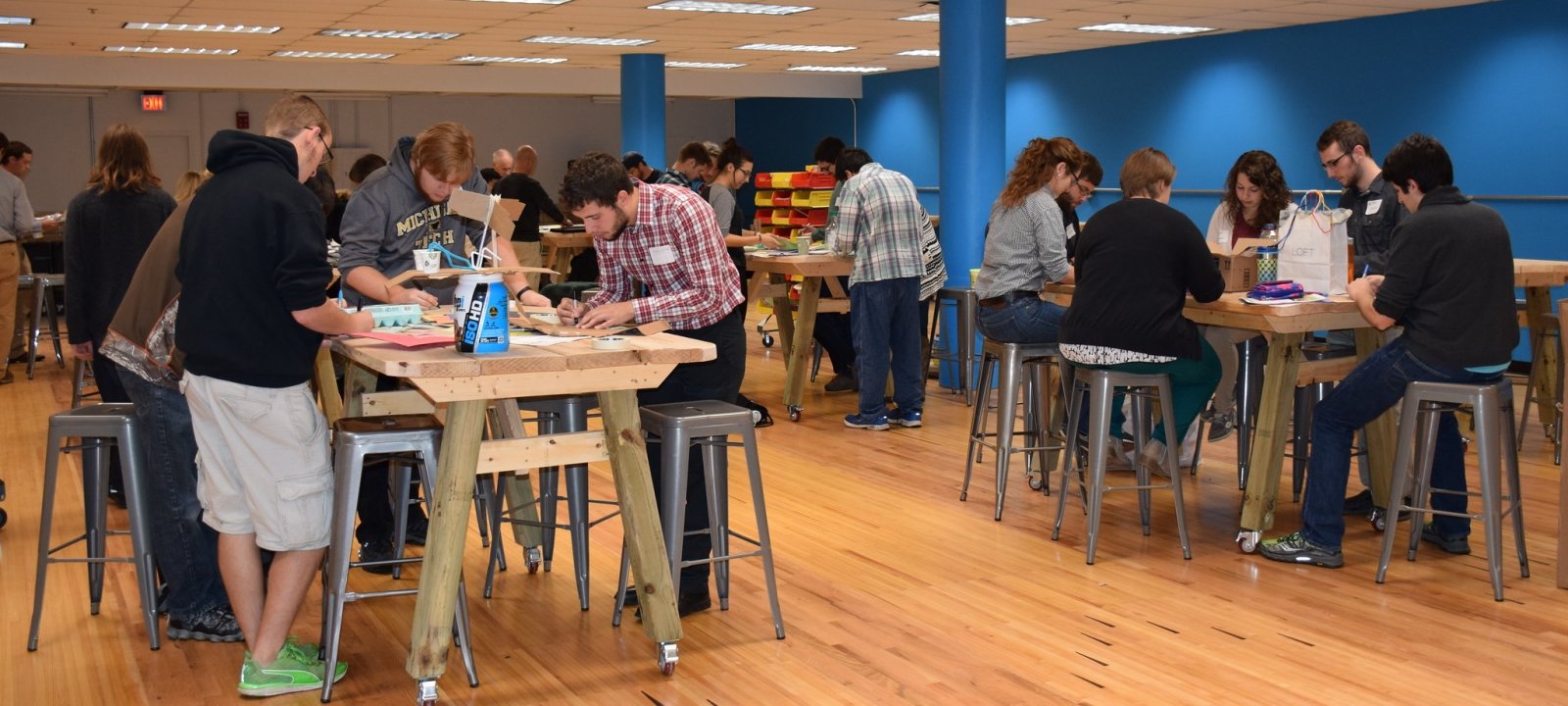 A group photo of students at the D80 conference working at tables in the Makerspace.