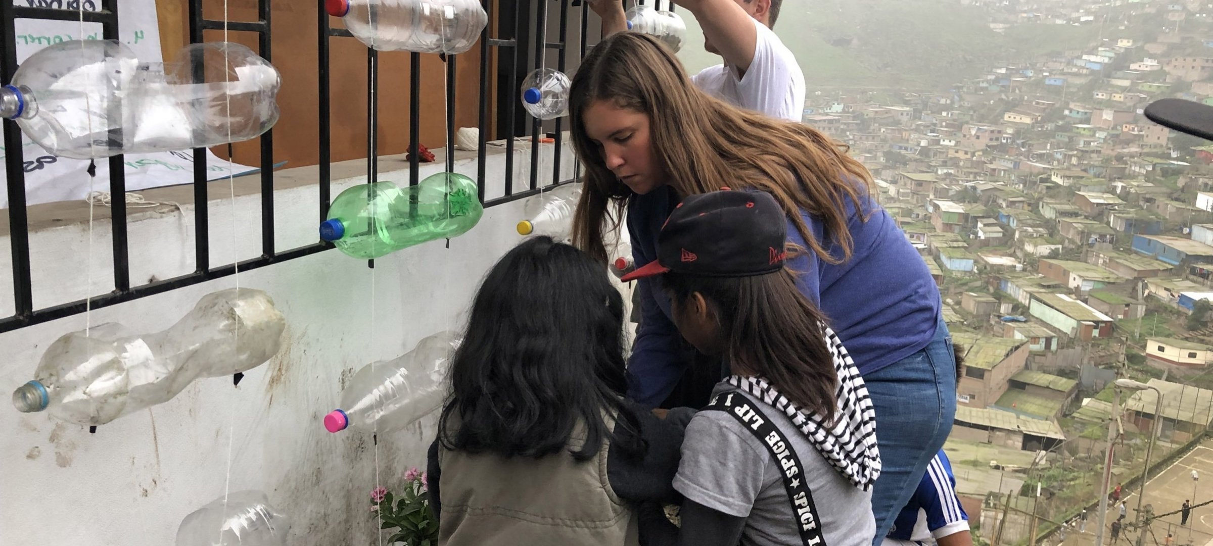 Image of a Michigan Tech student helping two young students with an art project while on a trip to Peru.
