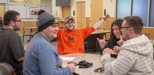 Five students sitting around a table, one has his arms raised in the air in celebration