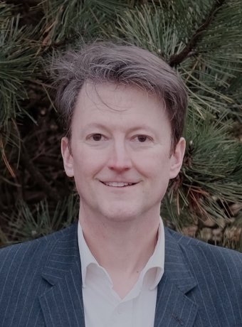 Portrait of Tim in a blazer in front of a pine tree.