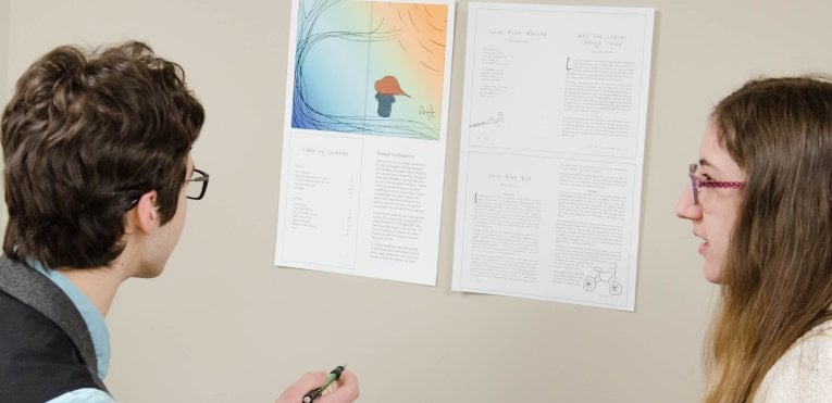 Two female students reviewing and editing a publication that is taped to the wall