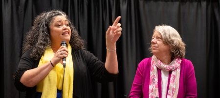 Speaker speaking with microphone with a person looking on