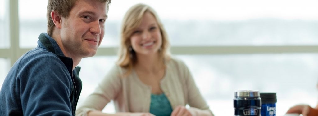 Two students sitting and looking at the photographer, smiling. 