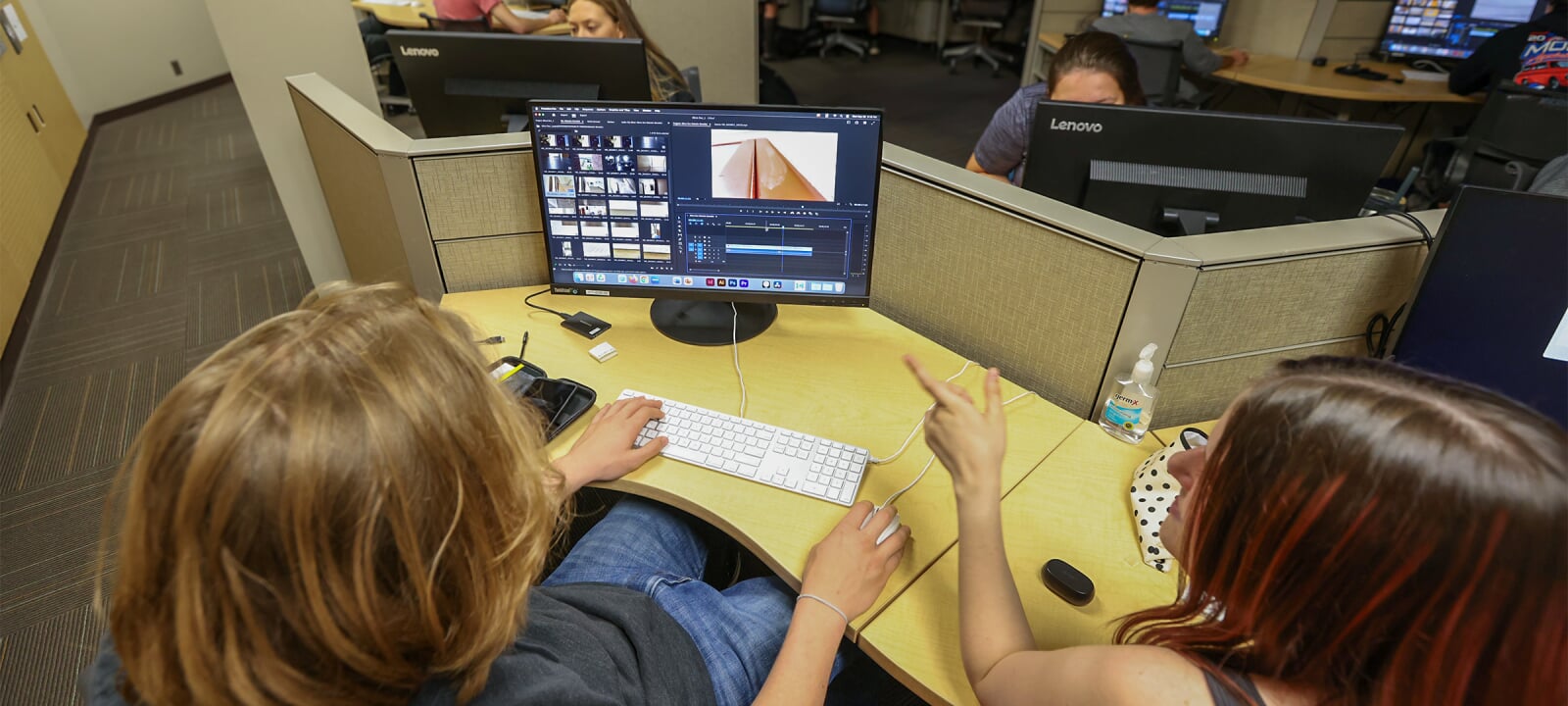 A view over the shoulder of two students collaborating at a computer while editing video in the Humanities Digital Media Zone.