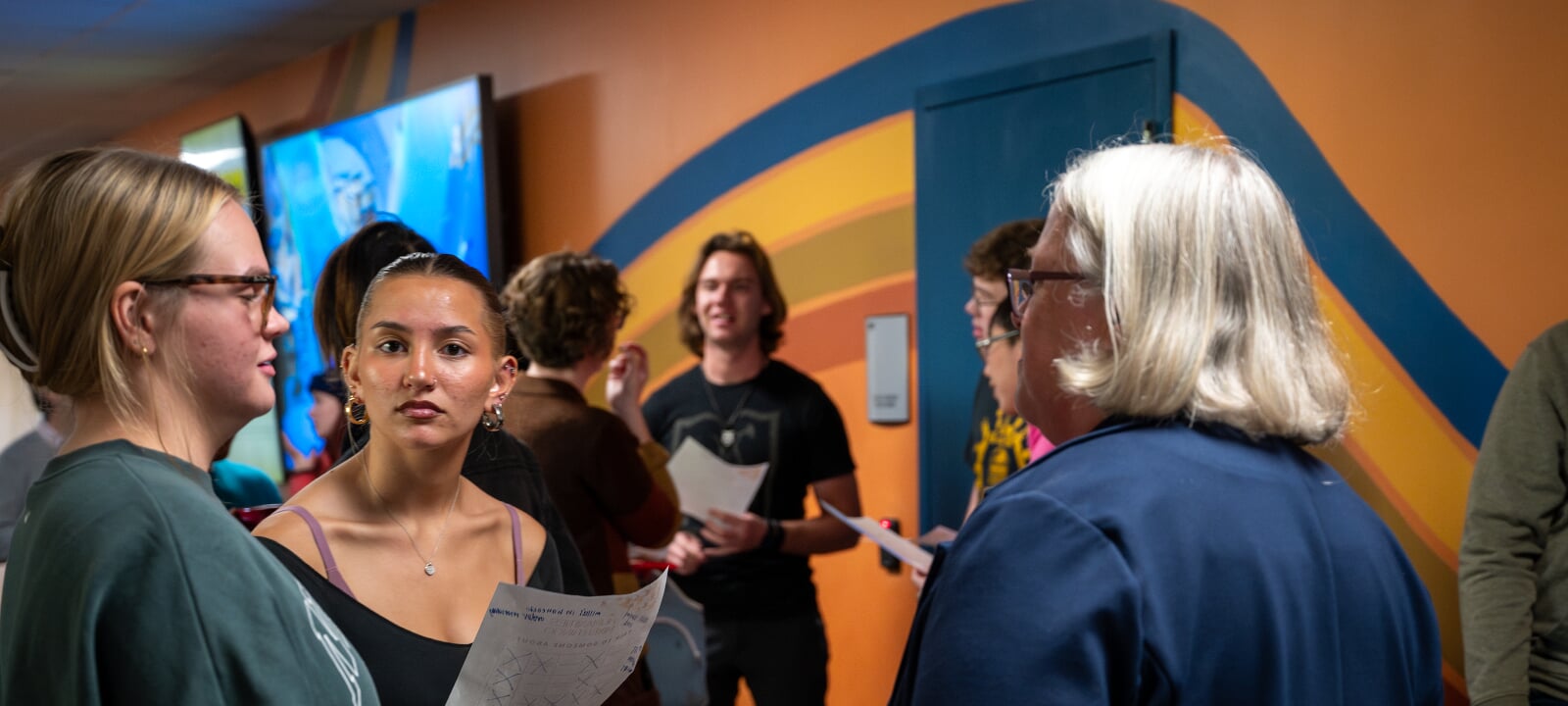 An Intro to Humanities student looks into a camera while her peers participate in a meet & greet in the third floor of Walker.
