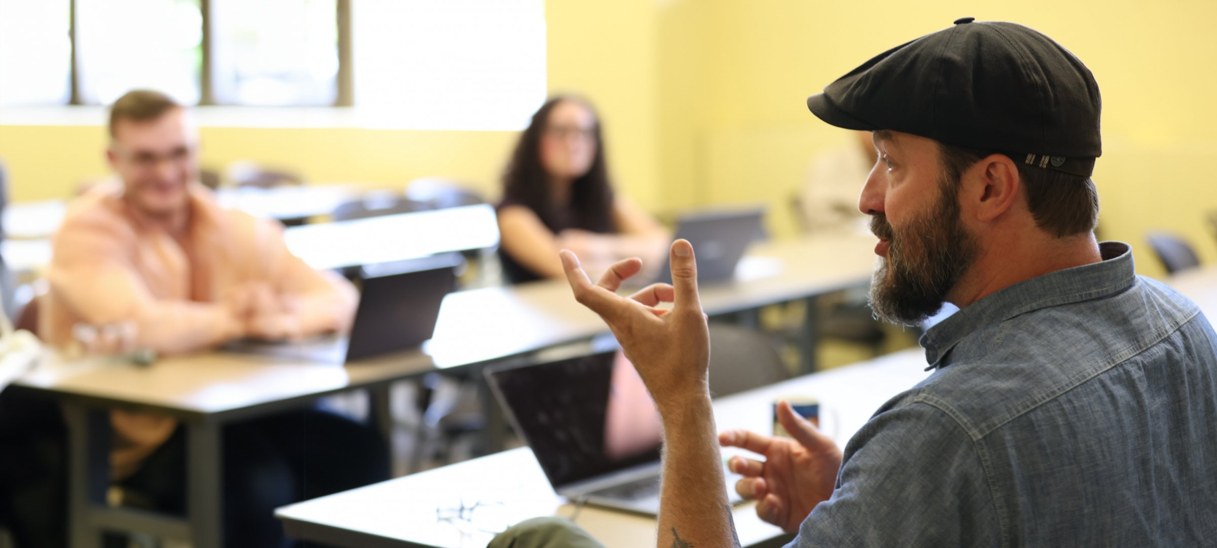 Writing Professor Matt Siegel lectures in the foreground with students looking on in the background.