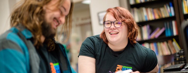 Two students sitting and laughing in the library of the Humanities department.