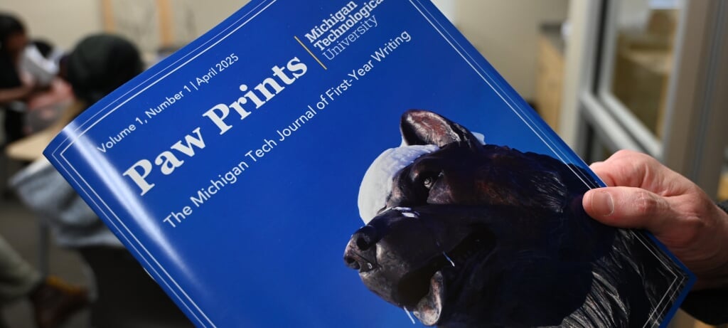 Hands holding the first issue of Paw Prints, dated April 2025, with a cover image depicting the campus husky statue against a blue sky.